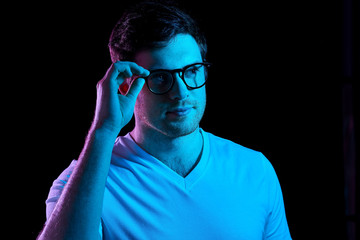 people concept - portrait of young man in glasses and t-shirt over ultra violet neon lights in dark...
