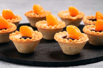 Sweet tartlets with chocolate and slices of tangerine on a dish of natural slate for serving