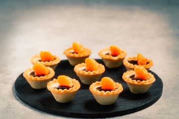 Sweet tartlets with chocolate and slices of tangerine on a dish of natural slate for serving