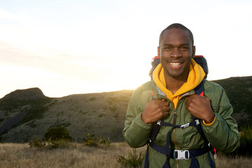 happy young african american man with with backpack smiling with sunrise in background
