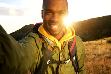happy black man hiking and taking selfie with sunset in background