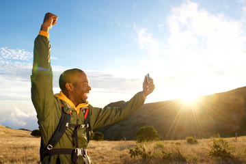 happy man hiking in mountains with arm raised when taking selfie with mobile phone