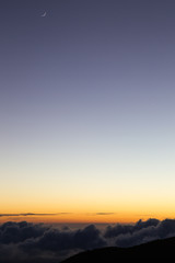 Crescent moon over the bright orange horizon lit by the last light of sunset at the Mauna Kea on Big Island, Hawaii, USA.