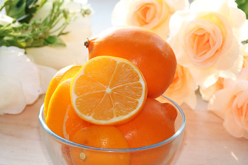 A lemon on a sunny table. A bouquet of cream roses in the background creates a good mood of a spring morning and a good day.;