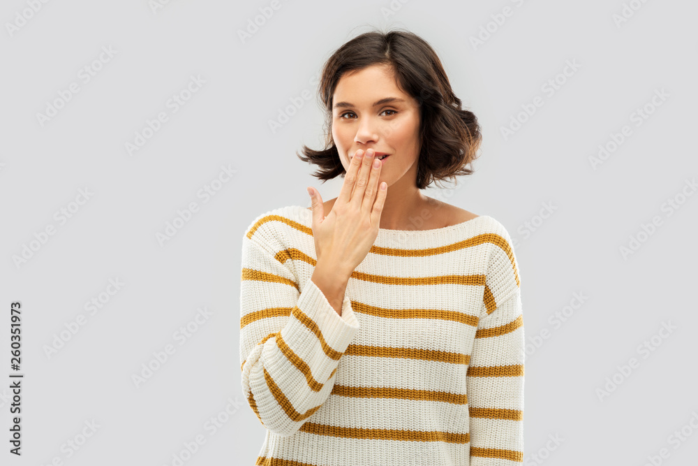 Sticker people concept - happy smiling young woman in striped pullover covering mouth by hand and giggling over grey background