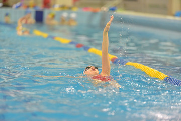 Young girl in goggles and cap swimming in the blue water pool