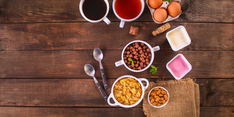 cornflakes, coffee, bread, butter, eggs, jam and other ingredients for breakfast on a dark background. Top view with copy space