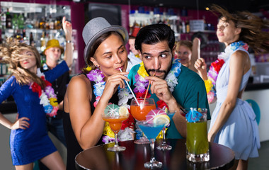 Man with woman in lei are drinking cocktails on party