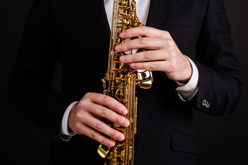 Naklejka premium Saxophonist in a black classic suit playing the soprano saxophone on a black background close-up