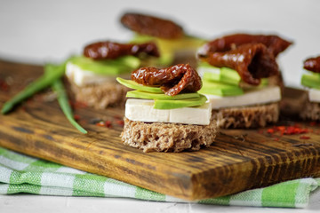 Appetizers with cheese, avocado and dried tomatoes on the board. Concept for food, healthy food and vegetarians.