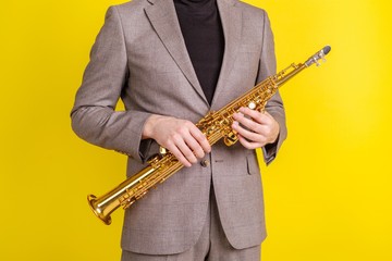 Saxophonist in classic clothes holding a soprano saxophone on a yellow background close-up