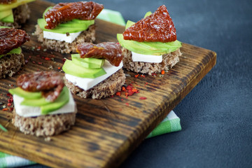 Snacks with cheese, avocado and dried tomatoes on a wooden board. Concept for food, healthy food and vegetarians.