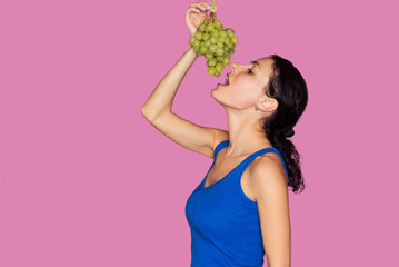 Portrait of young woman with fresh grapes isolated on pink background