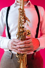 Saxophonist holding a soprano saxophone standing on a pink background close-up. Vertical photography