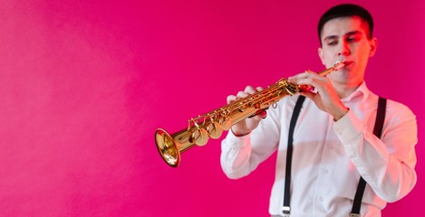 Male saxophonist who plays jazz on a soprano saxophone while standing on a pink background