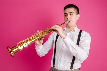 Fototapeta premium Saxophonist playing soprano saxophone standing on pink background