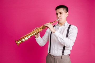 Male saxophonist playing soprano saxophone standing on pink background