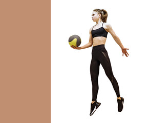 Full length portrait of a female in black sportswear and trainers jumping with a ball in her hand....
