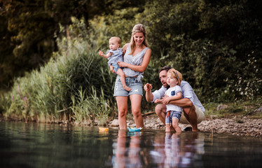 Young family with two toddler children outdoors by the river in summer, playing.