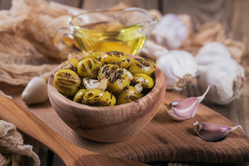 Grilled olives with garlic, olive oil and spices on rustic wooden table