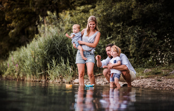 Young Family With Two Toddler Children Outdoors By The River In Summer, Playing.