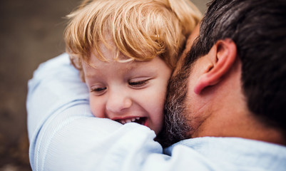 A close-up of father with a toddler boy outdoors by the river in summer.