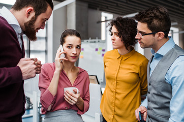 A group of young businesspeople with smartphone standing in office, making a phone call.