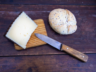 A wedge of cheese on a wooden board with an antique knife and rustic spanish bread