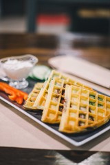 Belgian waffle sandwiches with baked tomatoes, cucumber, pepper and sauce served on a rectangular plate in a cafe