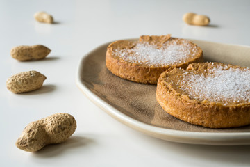 Dutch breakfast: rusk with peanut butter and sugar on brown plate. White table