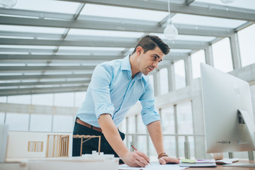 Young businessman or architect with model of a house standing in office, working.