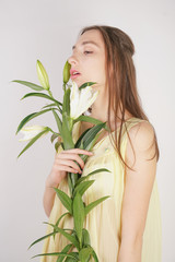 Naklejka premium a charming young caucasian girl in a retro yellow pleated transparent nightie holds a lush Lily flower in her hands and stands on a white background in the Studio