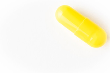 Capsule of yellow color on a white background. Minimalistic image suitable as a background on the theme of medicine and health.