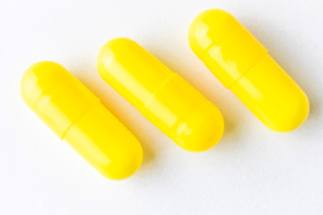 Three capsules of yellow color on a white background close-up. Minimalistic image suitable as a background on the theme of medicine and health.