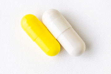 Yellow and white capsules on a white background close-up. Minimalistic image suitable as a background on the theme of medicine and health.