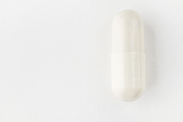 White capsule on a white background close-up. Minimalistic image suitable as a background on the theme of medicine and health.