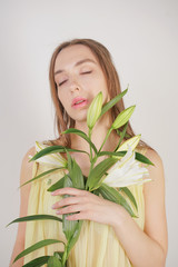 a charming young caucasian girl in a retro yellow pleated transparent nightie holds a lush Lily flower in her hands and stands on a white background in the Studio