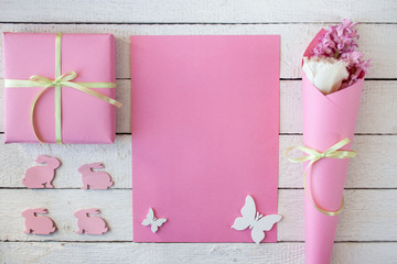 Różowo-białe tło z pudełkiem przewiązanym wstążką, kwiatami i zajączkami - obrazy, fototapety, plakaty