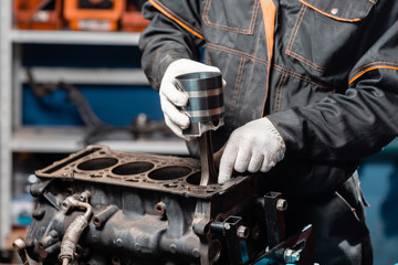 Car mechanic holding a new piston for the engine, overhaul.. Engine on a repair stand with piston...