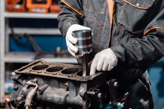 Car mechanic holding a new piston for the engine, overhaul.. Engine on a repair stand with piston and connecting rod of automotive technology. Interior of a car repair shop.