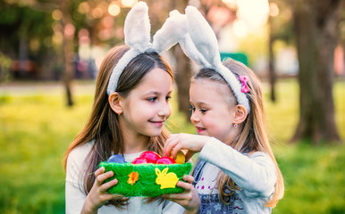 Easter. Two little girls with a bunny ears and colorful eggs have fun in the meadow