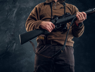 Close up view on a hands with rifle. Studio photo of a hunter against dark wall background