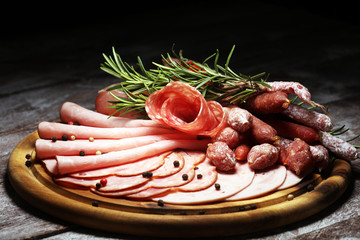 Food tray with delicious salami, pieces of sliced ham, sausage and salad. Meat platter selection.