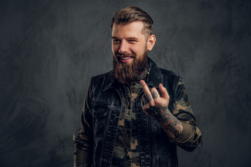 A crazy bearded man in the military shirt and denim vest with tattooed hands showing the fuck sign....
