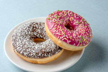 Two donuts on a white plate on a blue background.