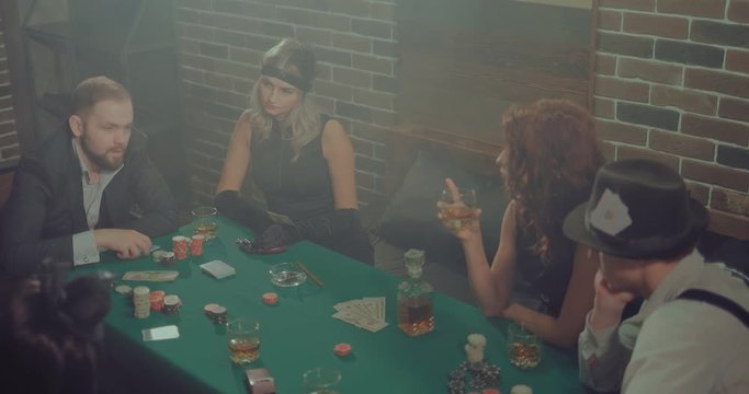 Beautiful and rich people are gambling. Man deals cards to players. Chips, money and cards are on the green table.