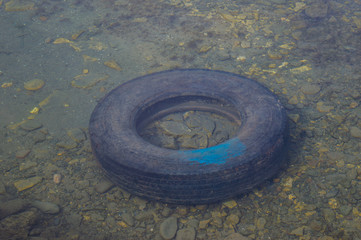 Car tire thrown in the clear water of a lake. Water pollution with a rubber tire.