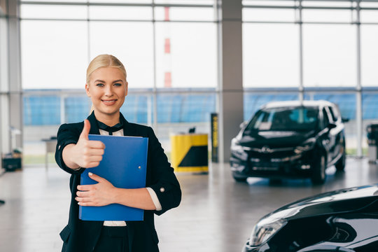 saleswoman showing thumb up in car showroom