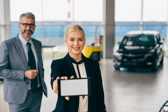 sales car agents holding tablet with blank white screen in car dealership showroom