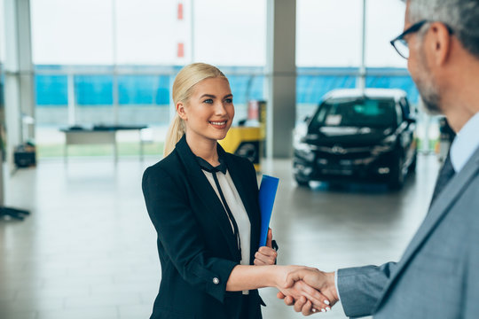 Saleswoman shaking hands with customer in car salon.
